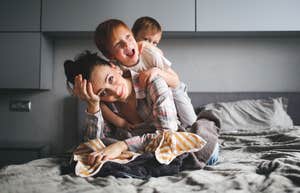 tired mother on bed with kids climbing on her back