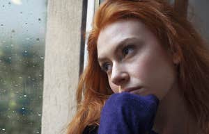 young woman looking sadly out a window