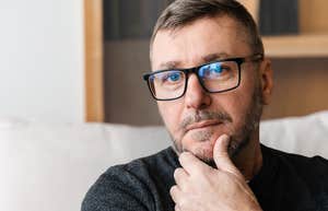 Subtle Signs Of A Man Who Has Been Through A Lot In Life, According To Research Older man holding his chin and looking seriously at the camera.