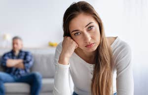 stressed wife looking annoyed while husband sits in background lazily