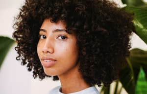 Positive Black woman with curly hair near green plants, confident and respected, showing subtle signs of true respect.