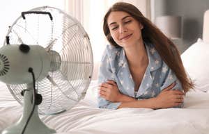 smiling woman laying in bed with fan blowing in her face
