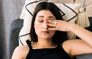 Exhausted woman rubbing her eyes on the couch, illustrating the quiet guilt people feel for resting due to habits learned in childhood.