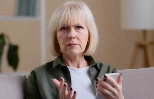 Serious older woman holding a phone on a couch becoming less patient as she ages