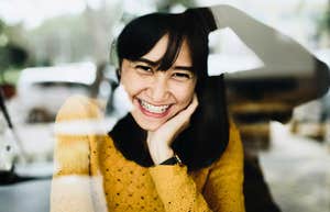 Woman smiling softly through a window with relaxed, genuine warmth, illustrating the subtle charm that helps people build instant goodwill with others.