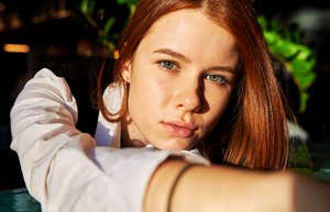 A woman gazes calmly toward the camera while extending her arm, conveying quiet boundaries and emotional distance.