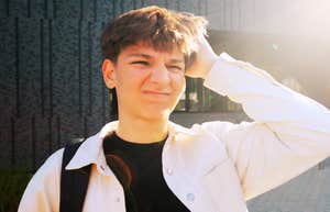 A preteen boy outdoors squinting, wearing a light jacket and backpack.