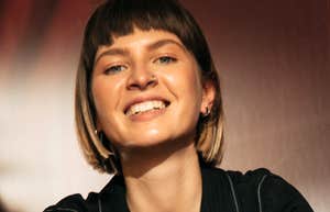 A woman with short hair smiles at the camera indoors under warm lighting.