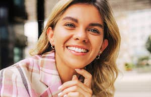 A woman smiling confidently while leaning forward outdoors.