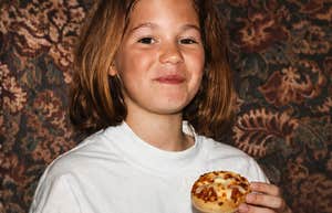 A child holding a small snack and smiling at the camera indoors