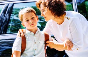 Every Morning My Son Shuts Down at Drop-Off — And I Can’t Reach Him concerned mother gently holding her young son by the shoulders near a parked car during school drop-off, boy wearing a backpack with withdrawn expression, bright morning light highlighting emotional tension and parental worry