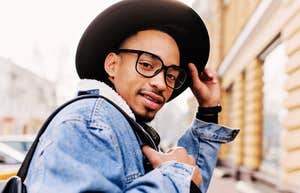 African man in trendy glasses and a denim jacket looking over his shoulder in a city setting, illustrating the mindset and small steps people take to bounce back after losing a job