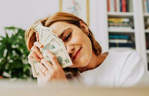 A woman with a joyful expression holding cash close to her face; illustrating the 