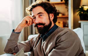 A thoughtful man sitting in a living room, looking away with a composed expression; a visual of the emotional self-regulation and focus characteristic of exceptionally resilient people.