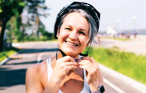 Rare Skills Of People Who Are Unusually Healthy In Ways Most People Don’t Even Notice Cheerful mature woman in a sports outfit fastening her bike helmet on a sunny day outdoors. She is standing on a paved cycling path, ready for a ride, showing an active and happy lifestyle.