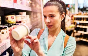 A portrait of a shopper checking product prices in a grocery store; illustrating the modern 'inflation math' strategy Americans are using to decide which food staples remain worth the increased cost.