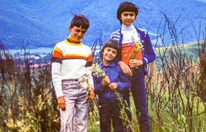 three boys from the 1960s and 1970s standing in the grass smiling