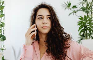 A portrait of a woman in professional pink attire looking focused while on a call; illustrating the non-verbal cues and 'soft power' strategies a career coach recommends for handling workplace rudeness.
