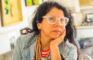 A Latin woman in her 40s or 50s attempting to work from home while appearing visibly drained; illustrating the 'double burden' of unpaid labor and professional demands that characterizes the Gen-X female experience in 2026.