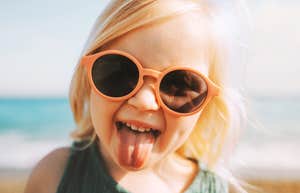 A young toddler girl playfully sticking out her tongue while posing in large sunglasses; illustrating the 'unshakeable self-esteem' and secure emotional foundation given to daughters by supportive, values-driven parents.