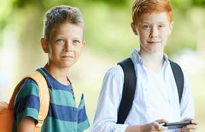 Two tween boys with backpacks, one using a phone 