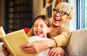 A grandma sharing a humorous moment with her grandchild over a children's storybook; illustrating 'cognitive vitality' and the spontaneous, late-life emotional healing found in intergenerational play.