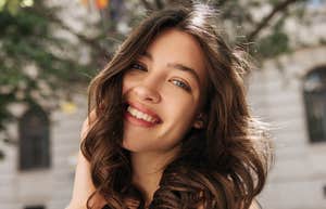 A close-up portrait of a serene young woman smiling softly while looking into the camera, with a blurred cityscape in the background conveying inner calm and emotional stability.