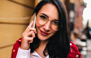 An outdoor photograph of a woman with red lipstick laughing while on a phone call, illustrating low-stress social connection, self-assurance, and high emotional regulation.