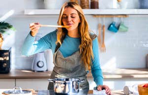 Surprisingly Simple Things People Who Actually Enjoy Cooking Usually Own woman who enjoys cooking tasting in her kitchen