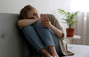 Woman sadly uses on her phone while alone on a couch