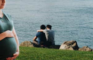 pregnant woman in front of gay couple embracing