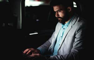 guy typing on laptop doing work at night in back of car