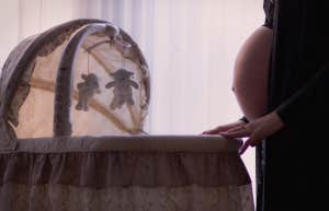 pregnant person standing over a crib