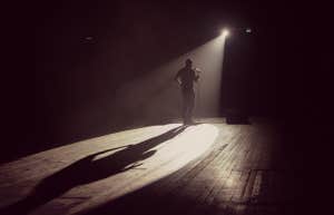 man on a stage doing comedy, backlit by spotlight 