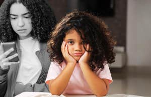 sad young girl in front of teen scrolling phone