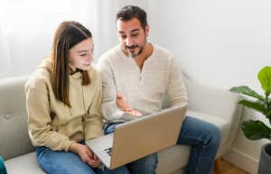 Dad Admits That His Daughter Will Not Pay For Her Own College Education And Will Have A Home & Car By The Time She's An Adult father and teen daughter sitting on couch and talking while looking at laptop