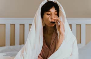 Woman covered by blanket, drinking wine 