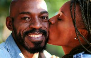 A woman kisses a man on the cheek as he smiles at the camera
