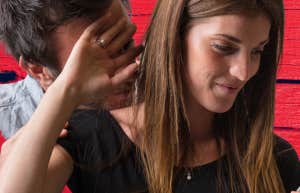 woman holding hand up smiling slightly while man tries to look at her phone