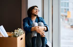 Distressed worker sits by a window with a box of his office things after losing their job.