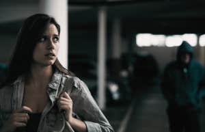 young woman in a parking lot looking concerned as someone follows her.
