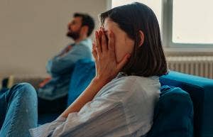 woman putting hand over eyes next to man on couch