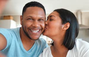 "She's my forever." A loving couple taking a selfie together at home. He smiles proudly, she kisses his check.