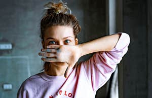 woman in topknot with big blue eyes and a pink hoodie covers her face