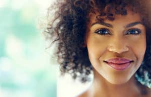 a content and happy woman looks at the camera, a slight burst of sunlight glows with her smile