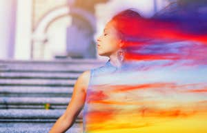 7 Ways To Ground Yourself When Daily Chaos Makes You Lose It a woman who is calm has a double exposure abstract colorful smear of light trailing behind her