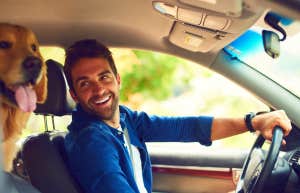 smiling man driving in his car with his dog