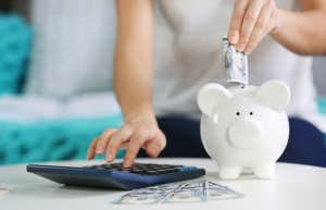 woman budgeting with calculator and putting money in piggy bank