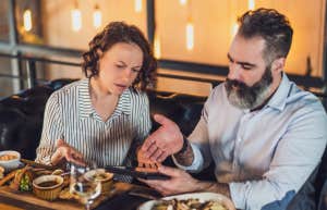 couple sitting at restaurant arguing over bill on tablet