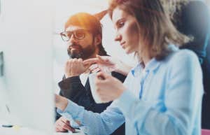 three people looking at a computer, a woman looking irritated while a man looks on 